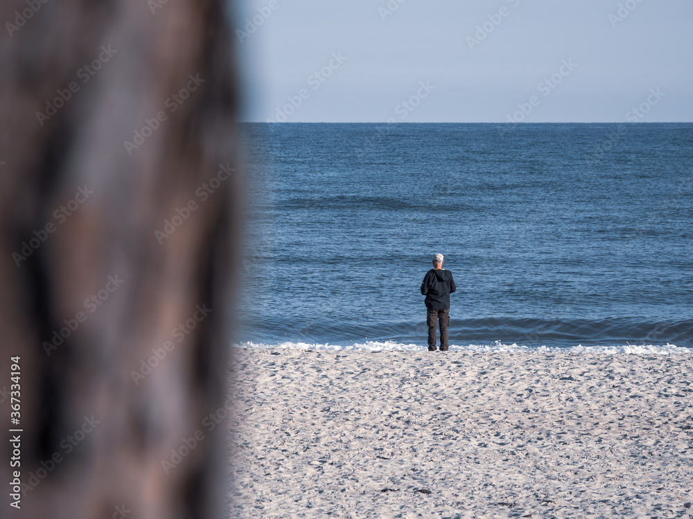  lonely man stands directly on the shore of a sea and looks at the water