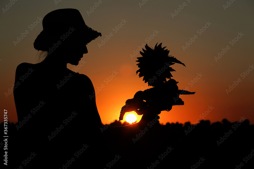 silhouette of a girl holding a sunflower photographed at sunset