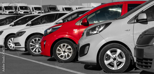 Black and white image of a row of cars. Only the red car has color