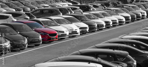 Black and white image of a row of cars. Only the red car has color