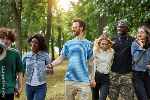 happy diverse african and caucasian people walk together in the park, have conversation and laugh. tolerance, international friendship concept