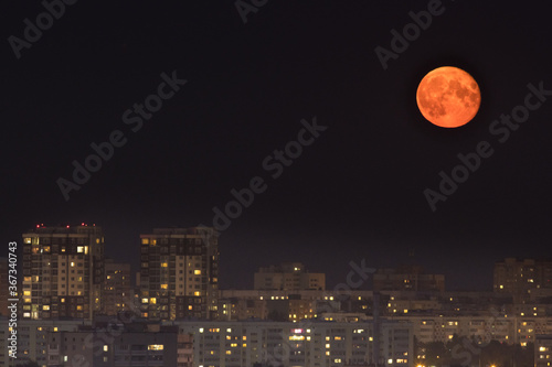 Bright yellow moon in dark night sky above the city