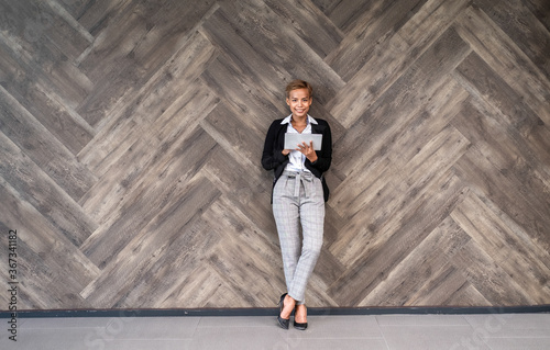 Smiling business woman holding tablet over brown wooden wall