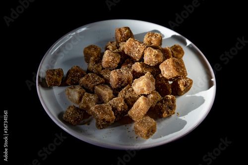 Brown sugar cubes on a white plate on a black background