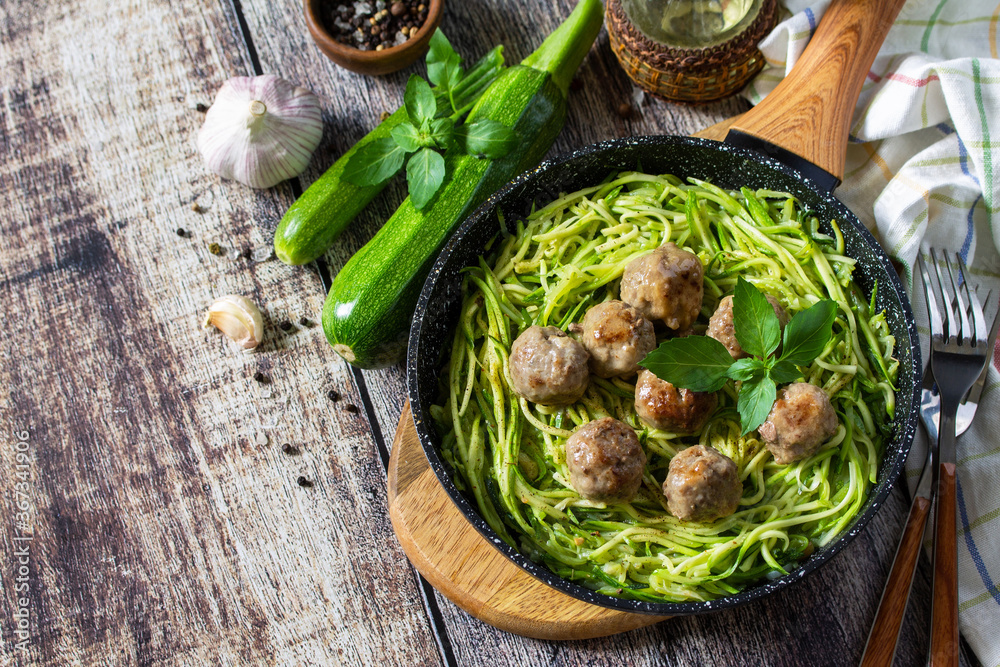 Healthy food. Cooked zucchini noodles with meatballs in a cast iron skillet on a rustic table. Copy space.