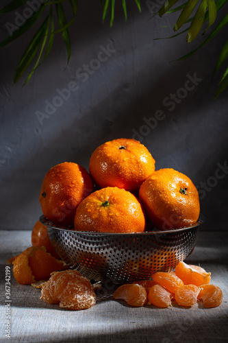 fresh juicy tangerines with drops of water in a metal colander and peeled tangerine slices lie side by side on a light linen tablecloth