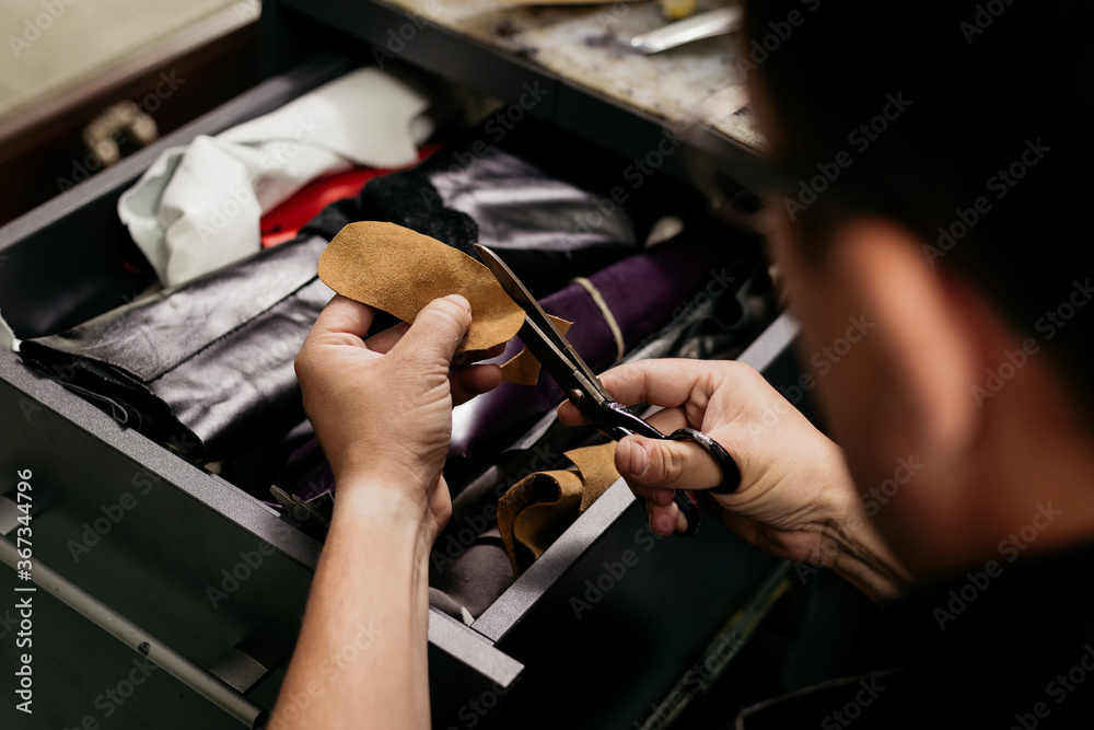 Obraz premium Male cobler sitting at his vintage looking shop and cutting leather fabric for shoe repairing