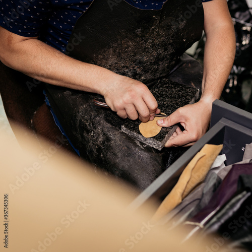 Male cobler sitting at his vintage looking workshop and cutting leather fabric for shoe repairing photo