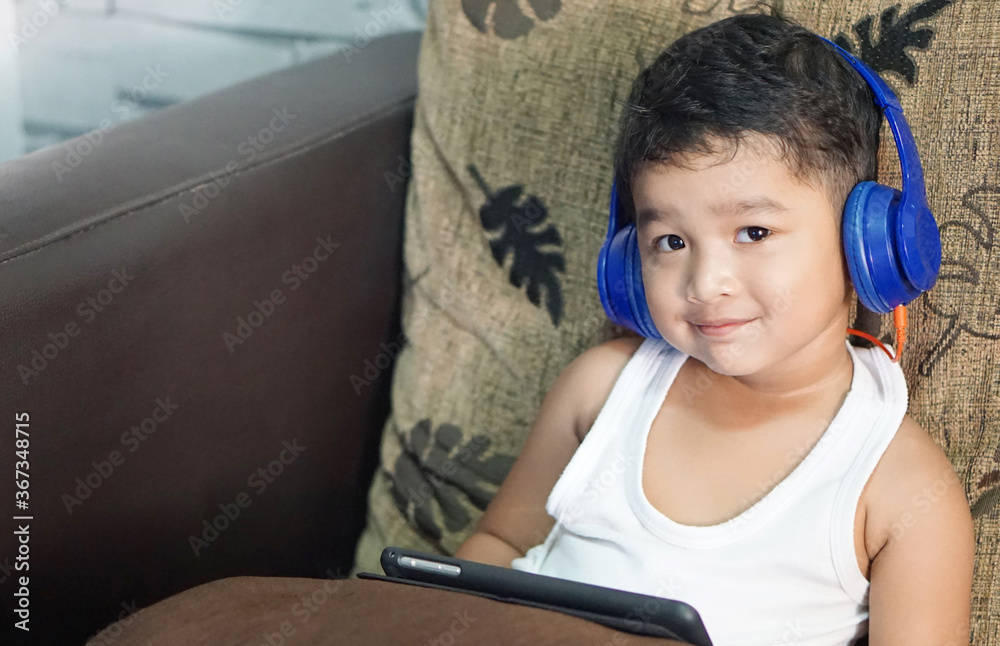 Cute Asian boy with headphones enjoys music on tablet, Keep your hands on the headphones concept. Cute Asian boy with headphones enjoys music on tablet, Keep your hands on the headphones concept.