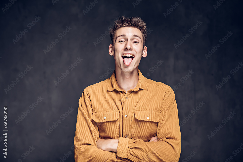 Young man sticking out tongue on dark background Young man sticking out tongue on dark background