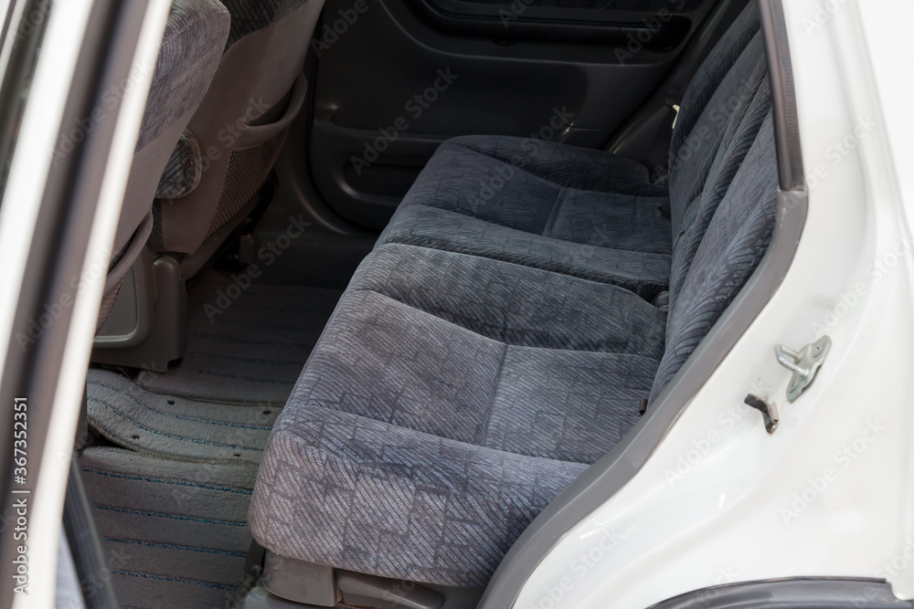 An open rear door of a white Japanese SUV overlooking a passenger row of seats made of gray textile material after dry cleaning before preparation for sale.