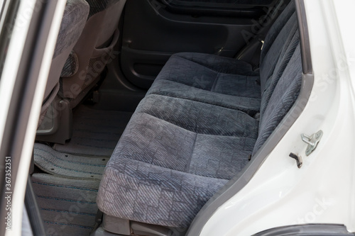 An open rear door of a white Japanese SUV overlooking a passenger row of seats made of gray textile material after dry cleaning before preparation for sale.