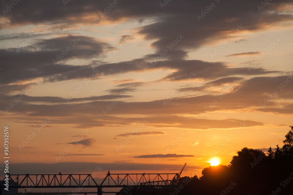 Picturesque landscape on the novosibirsk embankment with a silhouette of a railway bridge at sunset with an orange and blue sky.