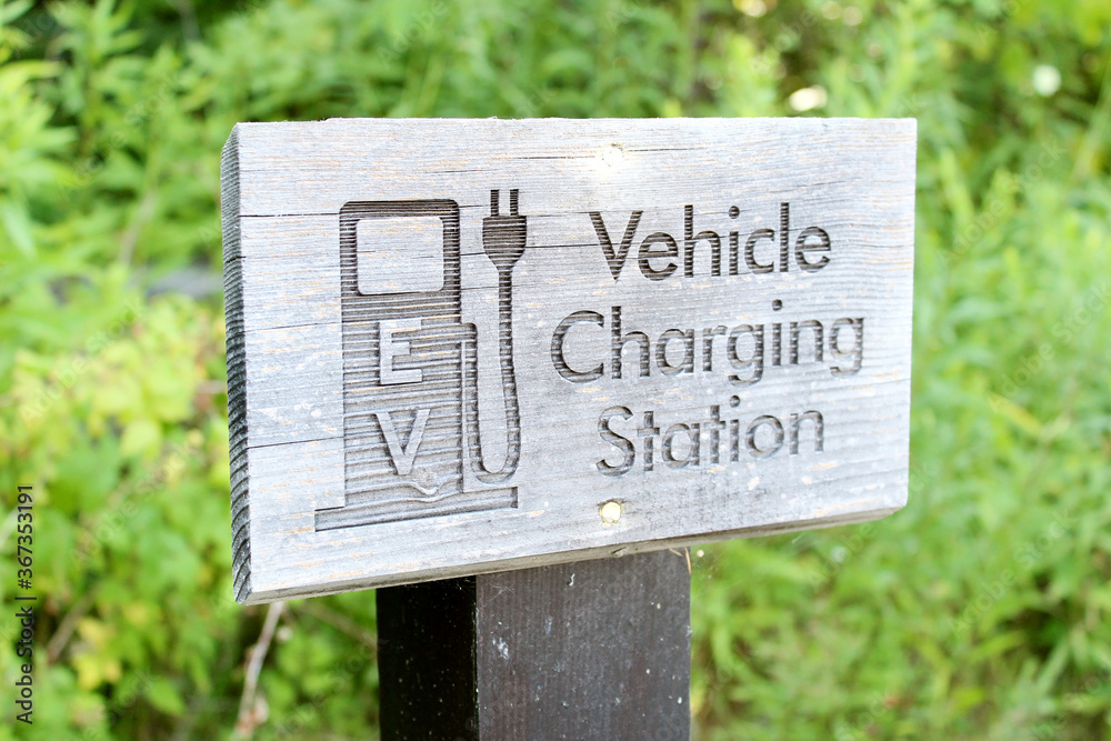 Wooden sign for electric vehicle charging with trees in the background.