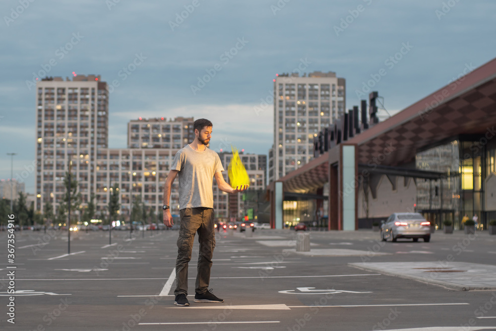 The guy is standing in the city on the street in the evening with a fire in his hand.