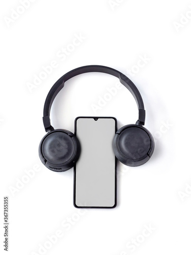 Black wireless headphone and mobile smartphone with a blank screen mockup lay on the surface of a white background