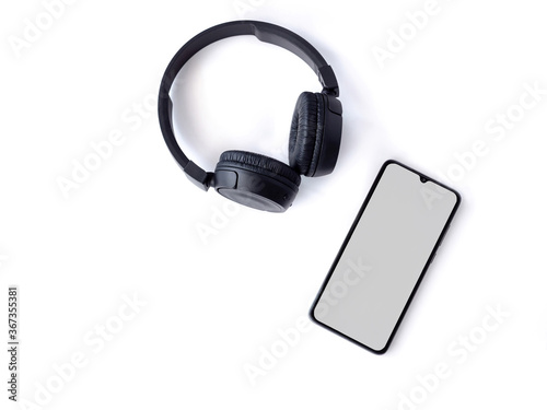 Black wireless headphone and mobile smartphone with a blank screen mockup lay on the surface of a white background