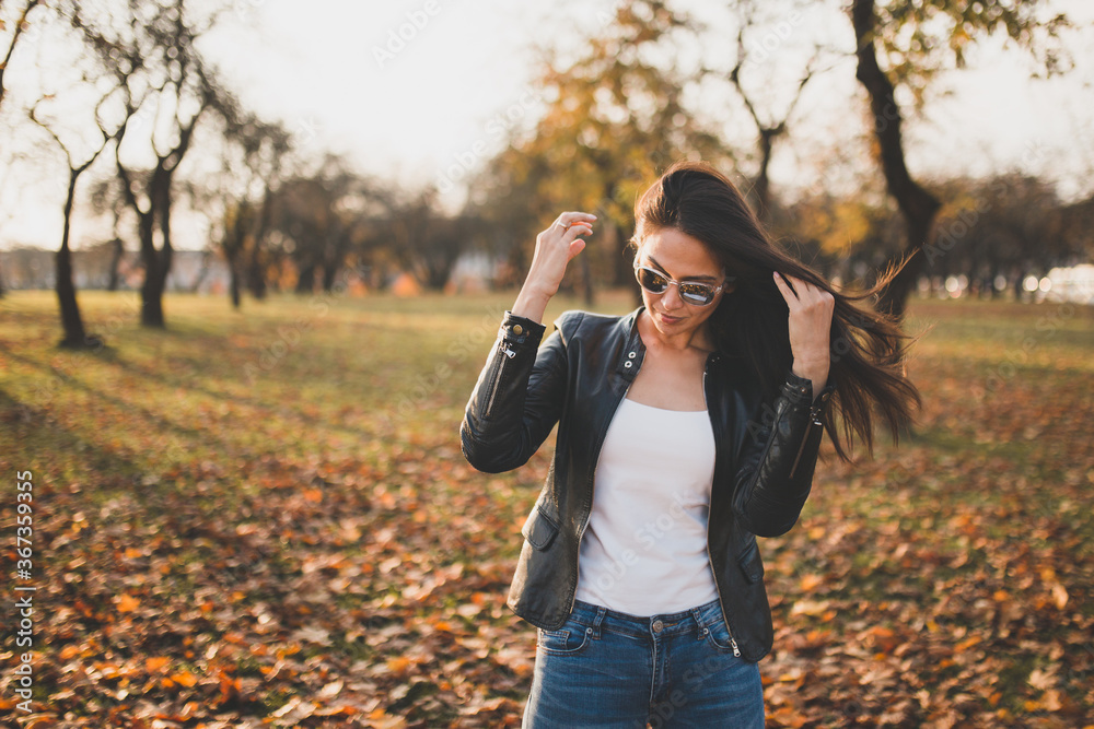 Attractive brunette girl in an autumn park straightens her hair in the wind - fall colors Attractive brunette girl in an autumn park straightens her hair in the wind - fall colors