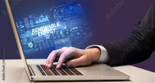 Businessman working on laptop with RENEWABLE ENERGY inscription, cyber technology concept