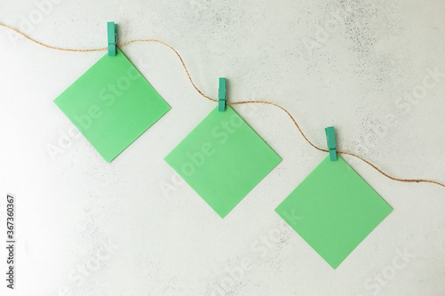 Green sheets of writing paper hang on colored wooden clothespins on a rope, on a white, battered background. Flat lay