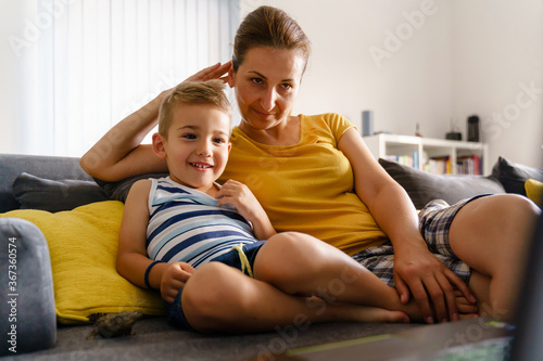 Small caucasian boy little child sitting on bed by mature woman - Mother and son at home watching content on laptop computer making video call having fun smiling - childhood leisure activity concept