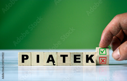 The hand turns the wooden cube and changes the polish word PIĄTEK (english friday)  with green positive tick check box and red reject X check box. photo