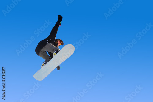 Snowboarder girl does a trick in jumping with a grab against the blue sky. Blue gradient background isolated athlete in flight