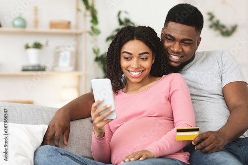 Happy pregnant couple using mobile application for shopping