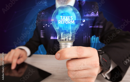 Businessman holding lightbulb with TAXES REFORM inscription, Business idea concept