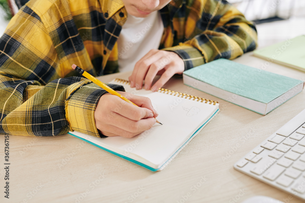 © DragonImages - Concentrated teenager making sketches for his school project in notebook