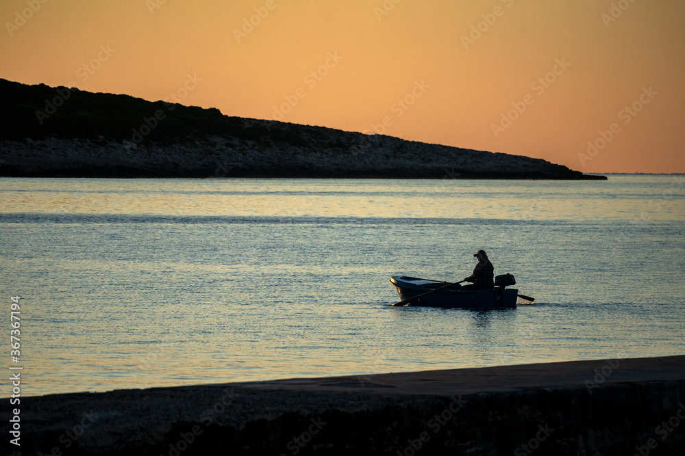 Silhouette of fisherman during angling from boat at sunset in quiet bay, on Island Vis in Croatia