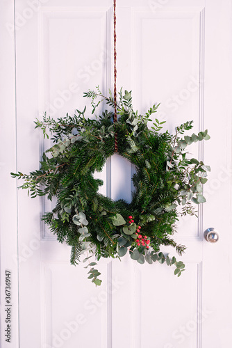 christmas wreath of fir branches and plants hanging on  white door, home decoration