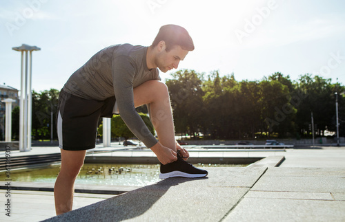 Start of marathon. Young handsome man tying shoelaces on steps