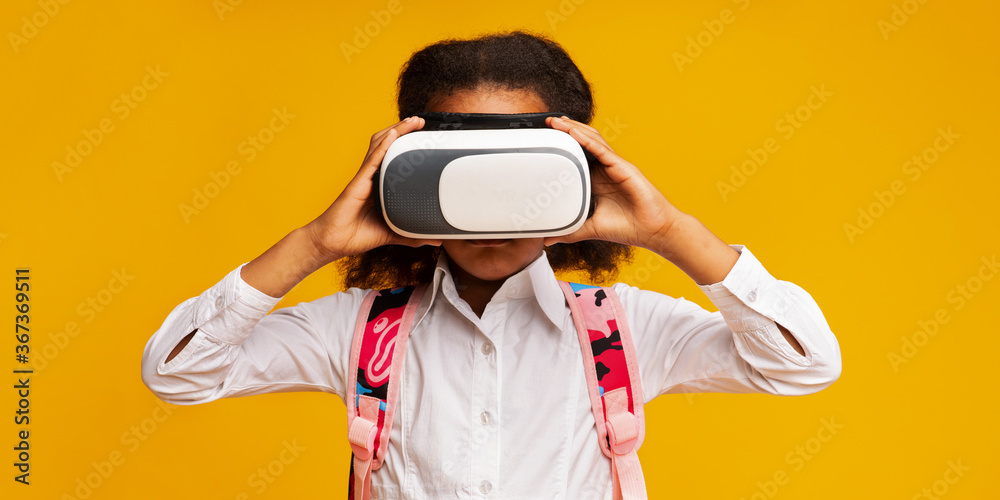 African Schoolgirl Wearing VR Glasses Experiencing Virtual Reality, Yellow Background