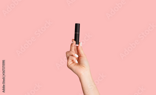 Beauty and makeup. Young lady holding tube of lipstick over pink background, closeup