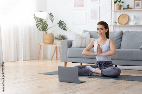 Positive yoga girl doing morning practice in front of laptop