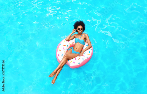 Enjoy summer. African American lady in swimwear floating on donut inflatable ring at pool  top view