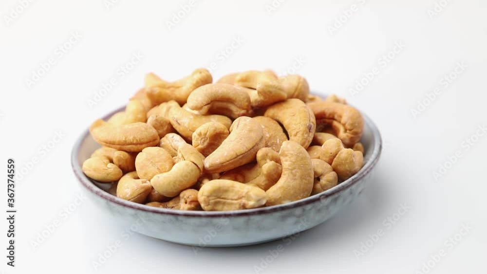Rotating of cashew in ceramic plate on white background. Side view, close up.