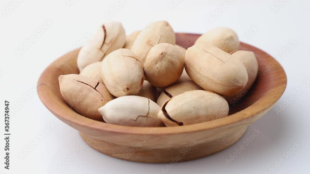 Rotating of raw pecan nuts in wooden plate on white background. Side view, close up. Rotating of raw pecan nuts in wooden plate on white background. Side view, close up.