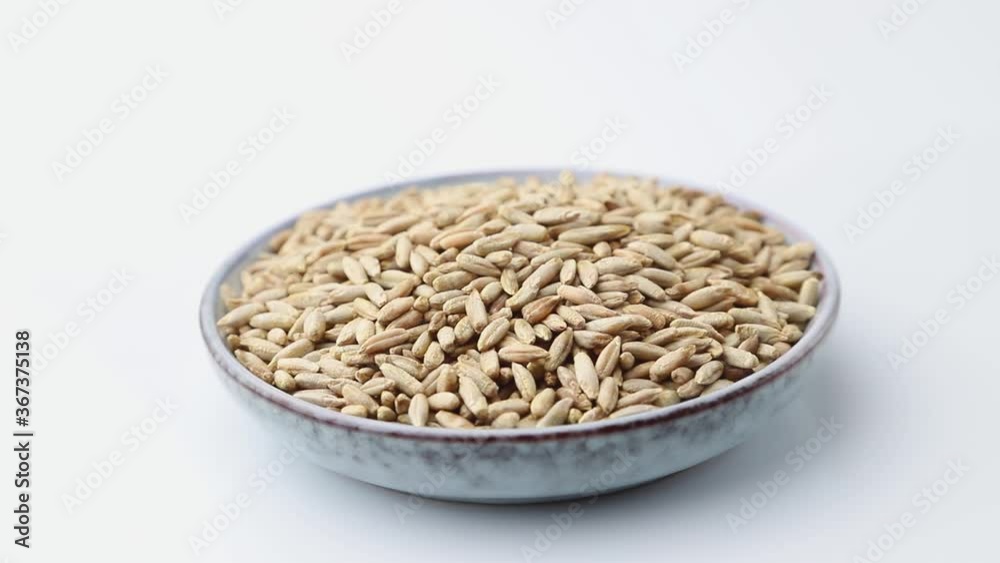 Rotating of rye grains in ceramic plate on white background. Side view, close up. Rotating of rye grains in ceramic plate on white background. Side view, close up.