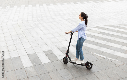 Smiling girl having pleasant ride on electric kick scooter