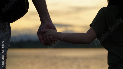 Father holding his daughter's hand, showing love during the sunset on a natural background. 
