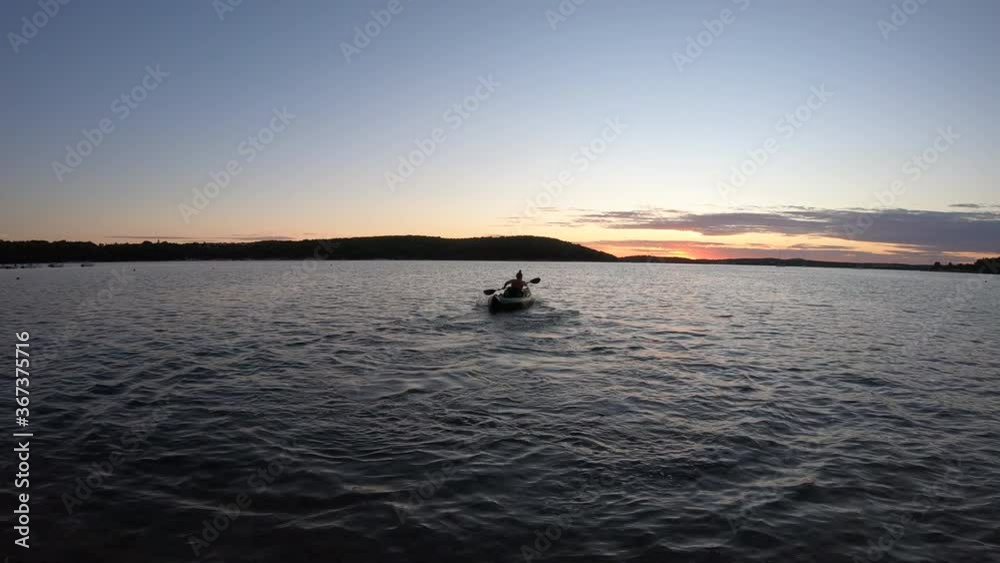 LD Wide shot of a young woman paddling a kayak at sea as the sun sets LD Wide shot of a young woman paddling a kayak at sea as the sun sets