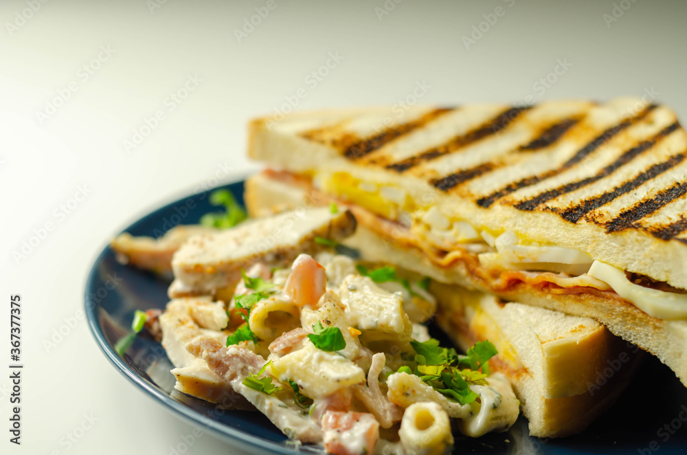 White bread with beechwood smoked bacon, egg, mayonnaise, and tomato served with Caesar pasta with parmesan cheese on the blue plate White bread with beechwood smoked bacon, egg, mayonnaise, and tomato served with Caesar pasta with parmesan cheese on the blue plate