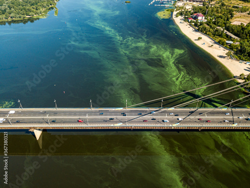 Cars travel along the North Bridge in Kiev. Green blooming algae in the Dnieper river on a hot summer day.