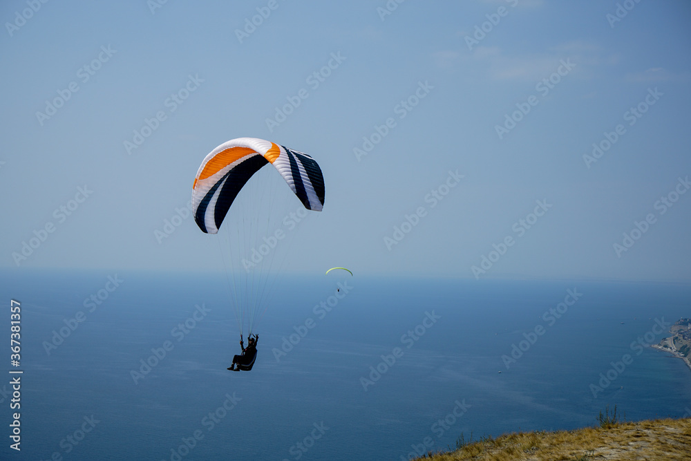 paragliders soar in the sky above the sea along the mountain range on a summer clear sunny day paragliders soar in the sky above the sea along the mountain range on a summer clear sunny day