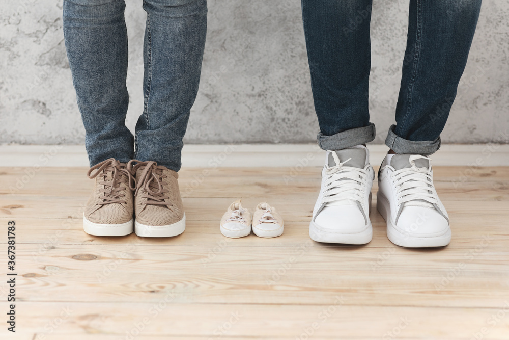 Male and female feet next to small baby shoes Male and female feet next to small baby shoes