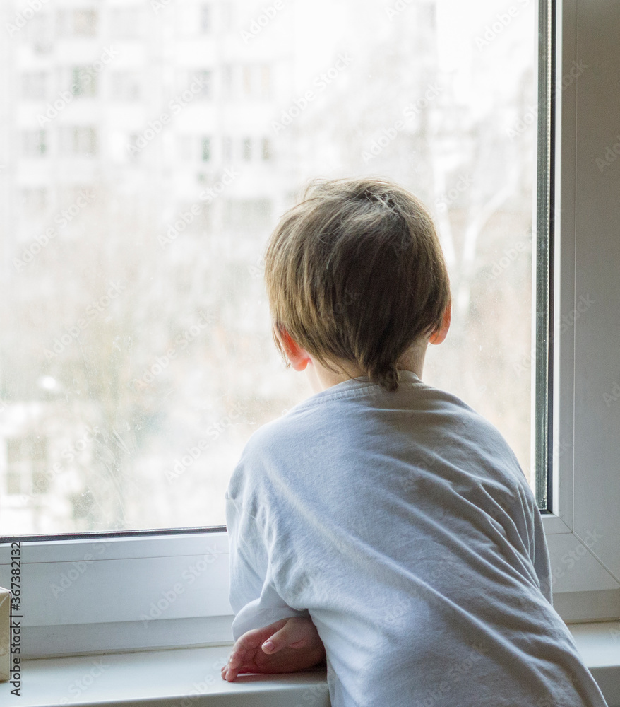 A little boy looks out the window. The street is bright and sunny. Cold weather A little boy looks out the window. The street is bright and sunny. Cold weather