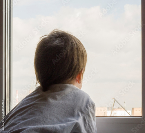 A little boy looks out the window. The street is bright and sunny. Cold weather