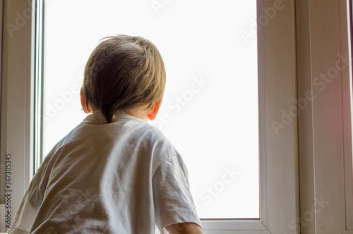 A little boy looks out the window. The street is bright and sunny. Cold weather